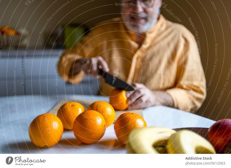 Älterer Mann, der zu Hause Orangen schneidet Senior Schneiden Messer orange Frucht Tisch frisch organisch Küche heimwärts vorbereitend Kaukasier