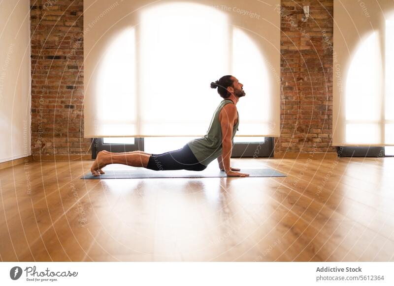 Mann übt Yoga in einem sonnenbeschienenen Raum Dehnung Unterlage Hartholzboden Sichtziegel natürliches Licht Pose friedlich Wellness Fitness Gesundheit Übung