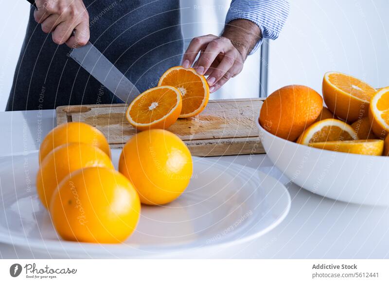 Unerkennbar Ernte Mann Koch in Schürze stehen und Schneiden von Orangen auf Schneidebrett in der modernen Küche Küchenchef Messer Hälfte geschnitten Frucht