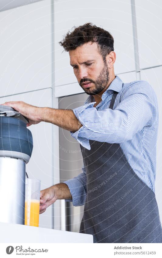 Niedriger Winkel eines erwachsenen Mannes in Schürze, der in der Nähe eines Tisches mit einer Orangenpresse in einer modernen Küche steht Küchenchef vorbereiten