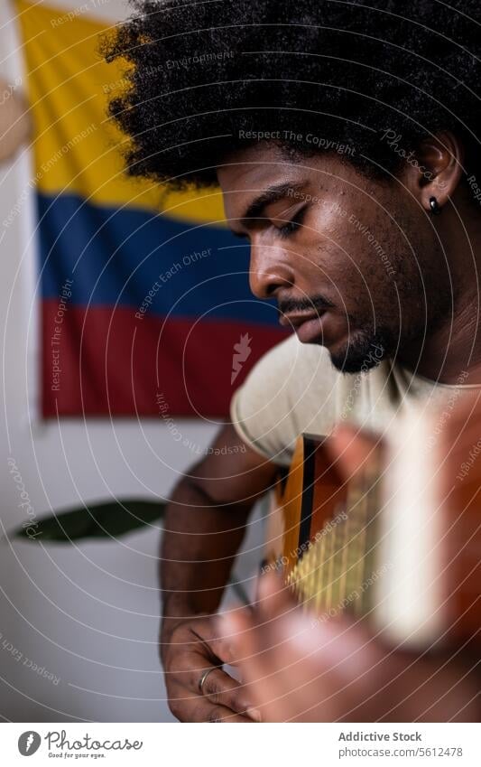 Ernster Mann spielt Gitarre zu Hause jung üben Porträt kolumbianisch Fahne selbstbewusst ernst Afrohaar sitzen spielen Fokus akustisch Schnur Instrument