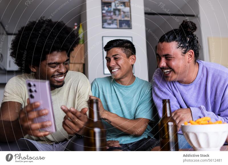 Männliche Freunde sehen ein Foto auf dem Smartphone zu Hause Lächeln Afrohaar Freizeit Zusammensein Wohnzimmer Freundschaft Wochenende Mobile Telefon Bier