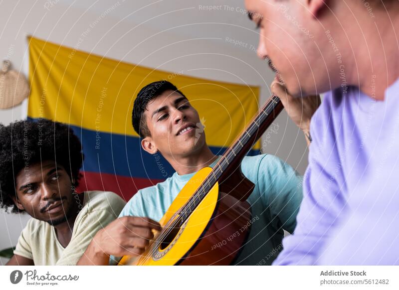 Männliche Freunde mit Gitarre und Fahne zu Hause heimwärts kolumbianisch Lifestyle Zusammensein Musik spielen sitzen von unten Blick Lächeln Freizeit Talent