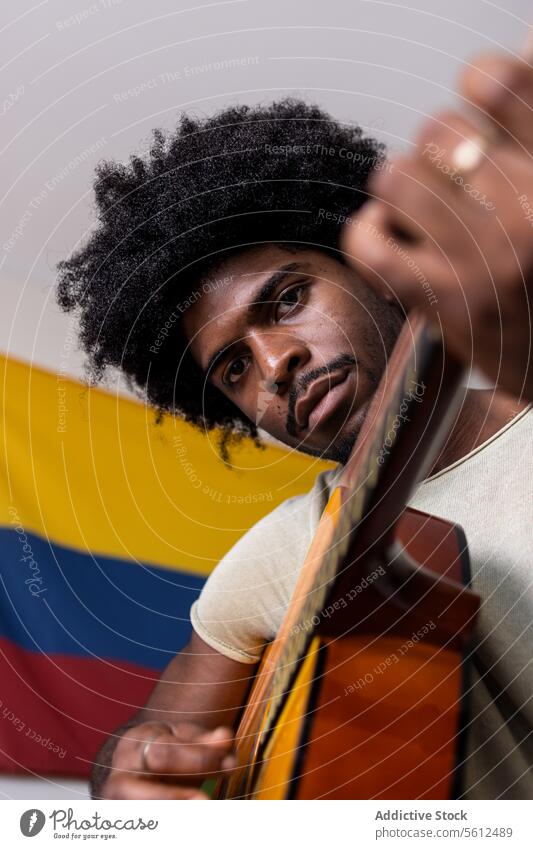 Ernster Mann spielt Gitarre zu Hause jung üben Porträt kolumbianisch Fahne von unten selbstbewusst ernst in die Kamera schauen Afrohaar sitzen spielen Fokus