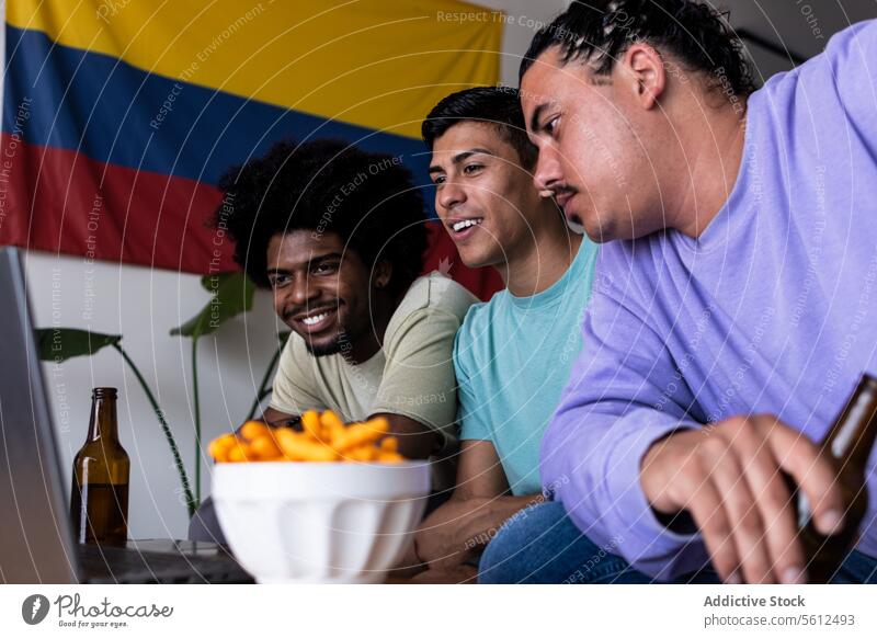 Glückliche männliche Fans, die das Spiel zu Hause am Computer verfolgen Freunde Lächeln Laptop Streichholz Sport aufgeregt Bier Flasche Snack zuschauend sitzen