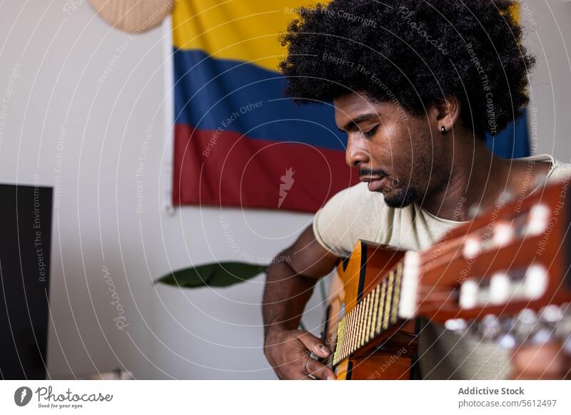 Ernster Mann spielt Gitarre zu Hause jung üben Porträt kolumbianisch Fahne selbstbewusst ernst Afrohaar sitzen spielen Fokus akustisch Schnur Instrument