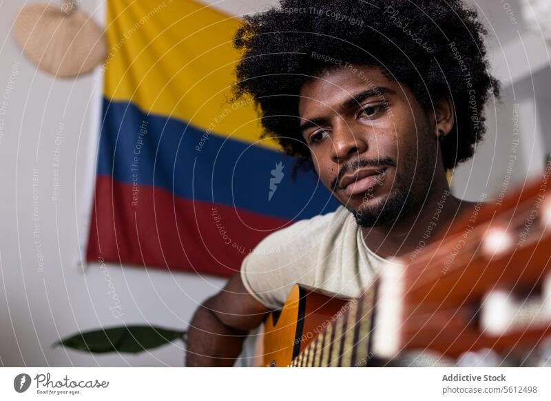Ernster Mann spielt Gitarre zu Hause jung üben Porträt kolumbianisch Fahne selbstbewusst ernst Wegsehen Afrohaar sitzen spielen Fokus akustisch Schnur