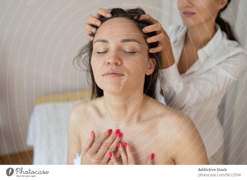 Crop-Hände einer nicht erkennbaren Masseurin bei der Haarmassage einer barbusigen Kundin, die die Therapie mit geschlossenen Augen in einem Spa genießt Kunde