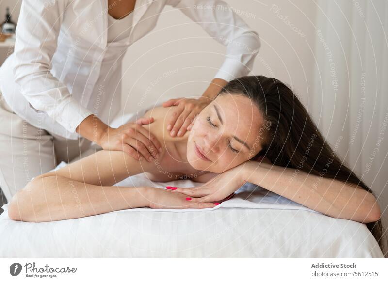 Schöne barbusige Kundin, die bequem auf einem Bett liegt und eine Rückenmassage von einem nicht erkennbaren Therapeuten in einem Spa-Salon erhält Kunde Massage
