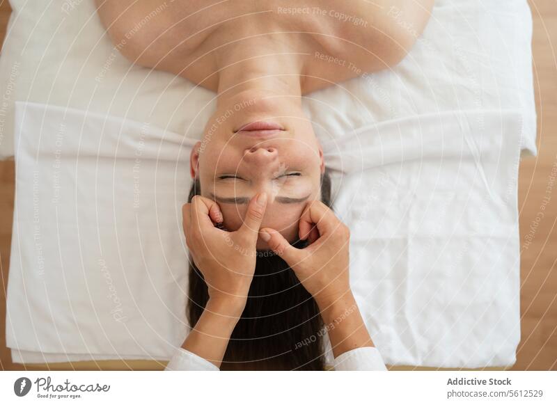 Hohe Winkel Ernte Hände von unerkennbaren Masseurin tun Gesichtsmassage zu weiblichen Kunden auf dem Bett liegend mit geschlossenen Augen in Spa-Salon Klient