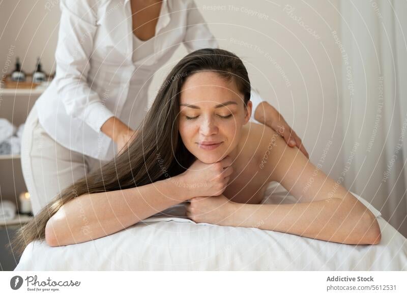Schöne barbusige Kundin, die bequem auf einem Bett liegt und eine Rückenmassage von einem nicht erkennbaren Therapeuten in einem Spa-Salon erhält Kunde Massage