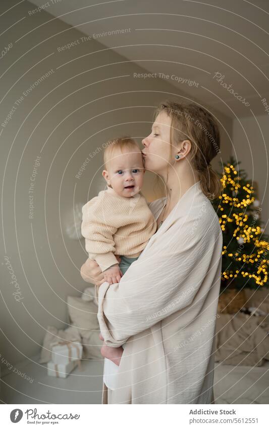 Zärtlicher Moment zwischen Mutter und Kind zu Weihnachten Baby Kuss Stirn Baum funkelnd Licht Angebot Liebe Pflege Zuneigung Familie Feiertag