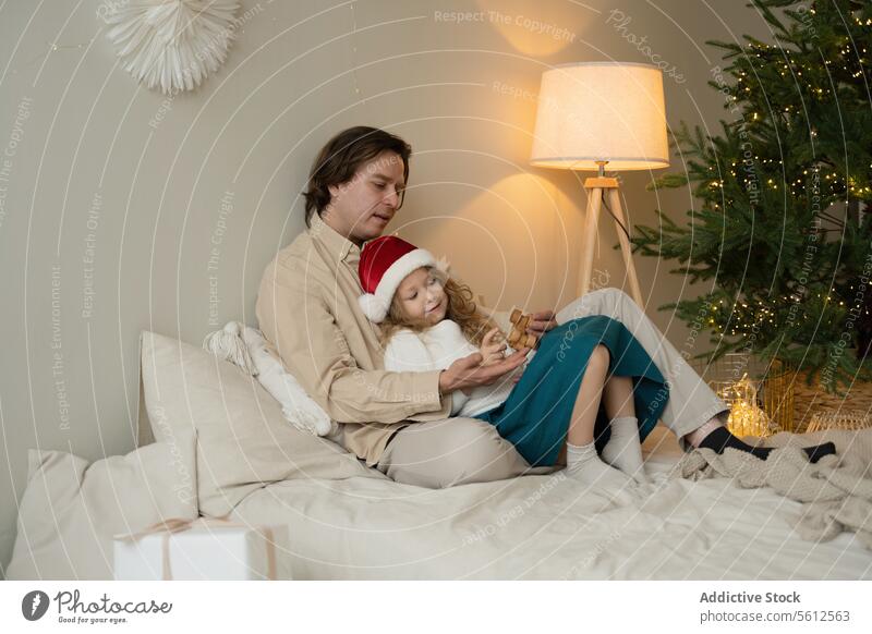Vater und Tochter genießen Weihnachten zu Hause heimwärts Weihnachtsmütze kuscheln Bett Weihnachtsbaum Angebot Moment Holzspielzeug Familie Feiertag festlich