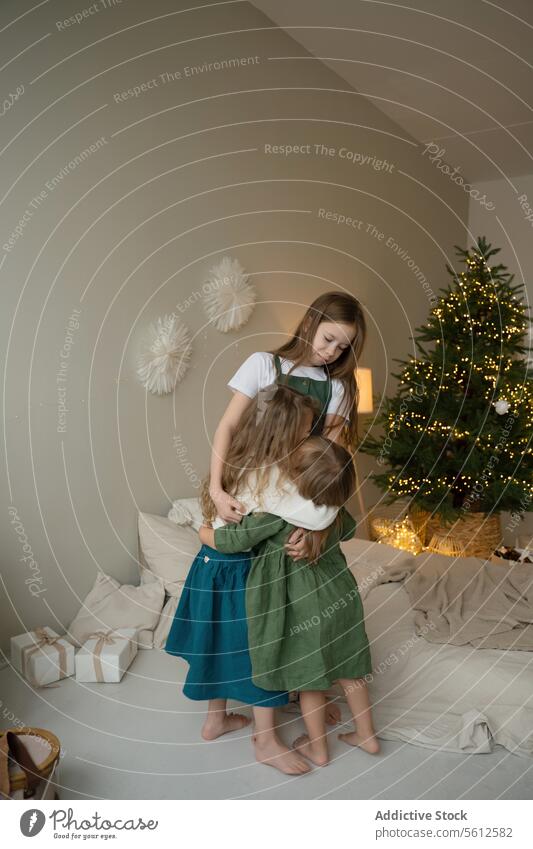 Zärtlicher Moment der Umarmung von Geschwistern am Weihnachtsbaum Mädchen Umarmen gemütlich Feiertag Wärme Familie Zuneigung Geschwisterkind Angebot jung Raum