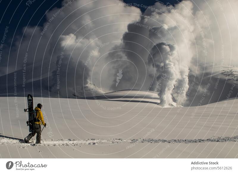 Unbekannte Person mit einem Snowboard, die in Richtung eines aktiven Vulkanausbruchs in einer verschneiten japanischen Landschaft läuft Eruption Schnee Winter
