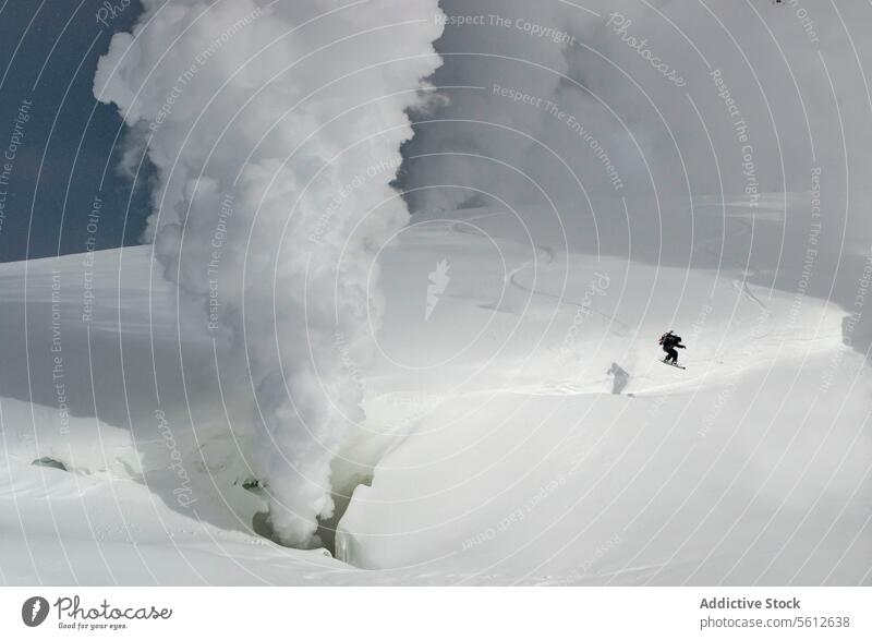 Ganzer Körper der aktiven unerkennbaren Person Snowboarden auf Schnee bedeckten Berghang mit Vulkanausbruch im Hintergrund während sonnigen Tag im Winterurlaub