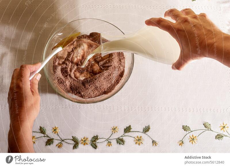 Draufsicht auf eine anonyme Person, die Milch in eine Schale mit Schokoladengeschmack auf dem Tisch gießt Frühstück melken Gießen Schalen & Schüsseln Kannen