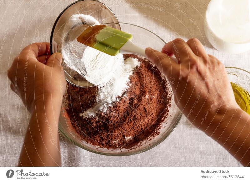 Draufsicht auf eine Backzubereitung mit den Händen einer nicht erkennbaren Person, die Mehl in eine Schüssel mit Kakaopulver schüttet Hand Schalen & Schüsseln