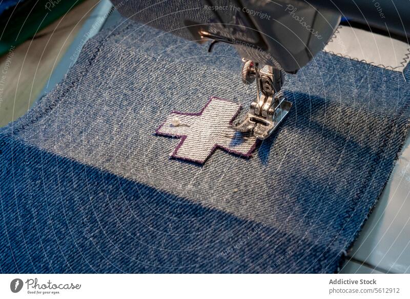 Nähmaschine näht einen Aufnäher auf Jeansstoff Nähen Maschine Näherei Fleck Gewebe Nadel Faser Textil blau weiß durchkreuzen Nahaufnahme Detailaufnahme Handwerk