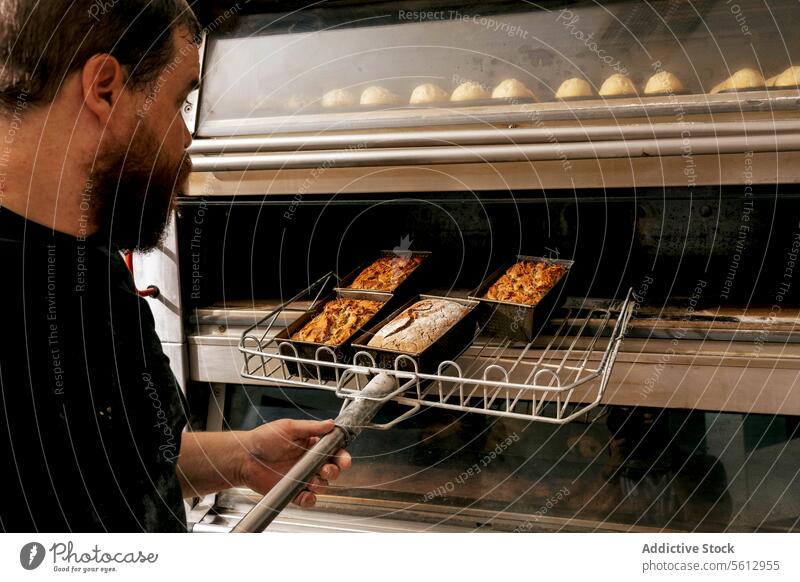 Bäcker nimmt heißes Backgut aus dem Ofen Küchenchef Bäckerei Lebensmittel Brot Gebäck Konzentration Freizeitkleidung gebacken Knusprig erwärmen metallisch