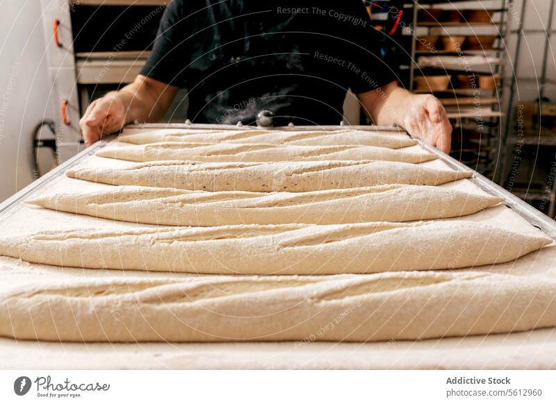 Mann trägt Tablett mit Brot in einer Bäckerei Teigwaren roh Brotlaib Küche Ernte unkenntlich schwarz T-Shirt vorbereiten Herstellung Hand Lebensmittel