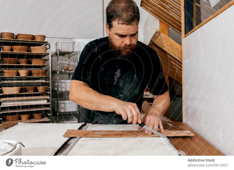 Koch schneidet Teig in der Bäckerei Schneiden Teigwaren hölzern Werkzeug Messer Fokus ernst Konzentration Tisch Gebäck ungekocht Utensil Schimmelpilze