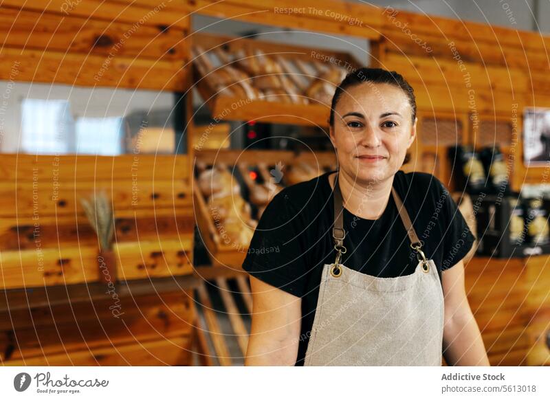 Glückliche Verkäuferin neben Brot in einer Bäckerei Regal Brotlaib selbstbewusst Lächeln Schürze frisch gebacken Lebensmittel hölzern Abfertigungsschalter