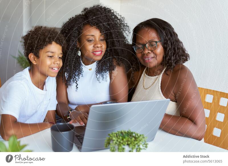 Frauen mit Teenagerjungen zu Hause Junge Laptop Kaffee Becher Lächeln Tisch Lifestyle Afro-Look Mutter Großmutter Sohn Tochter Enkel Sitzen heimwärts trinken