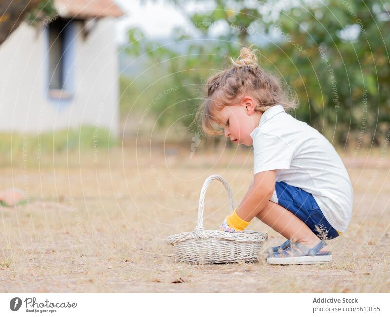 Seitenansicht eines kleinen Jungen, der im Garten hockend in einen Weidenkorb schaut Kommissionierung Korb Hinterhof Gartenarbeit Urlaub niedlich Kindheit