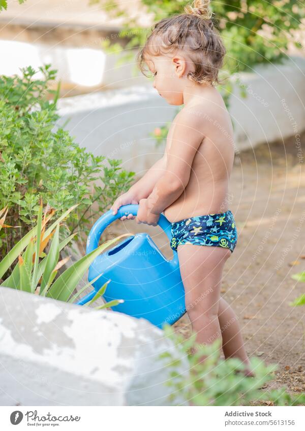 Seitenansicht eines kleinen Jungen ohne Hemd, der in den Ferien mit einer Gießkanne frische Pflanzen im Garten gießt Bewässerung Dose grün Wasser Sommer Urlaub