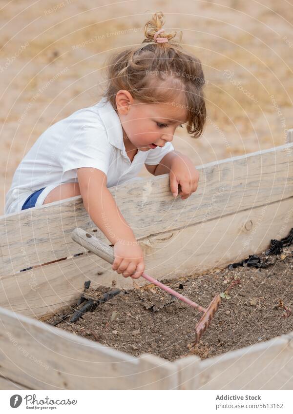 Seitenansicht eines kleinen Jungen, der eine Harke in einem Hochbeet im Hinterhof benutzt Boden Garten Bepflanzung Urlaub niedlich Gartenarbeit Beteiligung