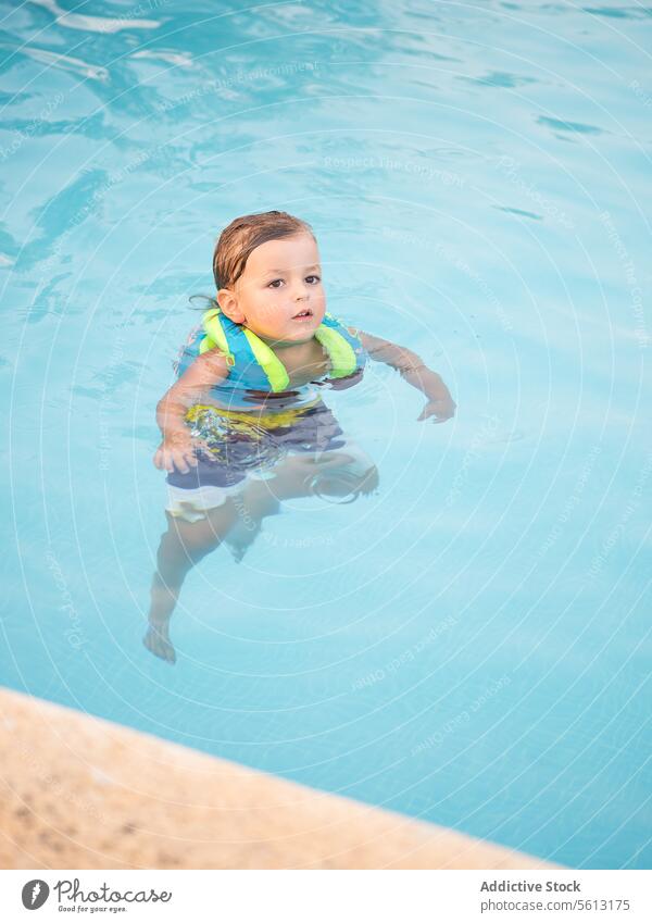 Hohe Winkel von Cute Junge trägt aufblasbare Jacke beim Schwimmen im Pool Schwimmsport niedlich spielerisch fliegend Wasser Kind Sicherheit Lifestyle Erholung