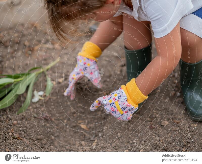 Anonymer Junge in Freizeitkleidung und Handschuhen sammelt Erde bei der Gartenarbeit im Hinterhof Beteiligung Boden Lernen Blatt Stiefel gesichtslos Kind