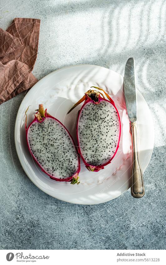 Frische Drachenfruchthälften auf einem weißen Teller mit Messer Schatten Textur Tisch altehrwürdig Silberwaren frisch geschnitten pulsierend Hälften tropisch