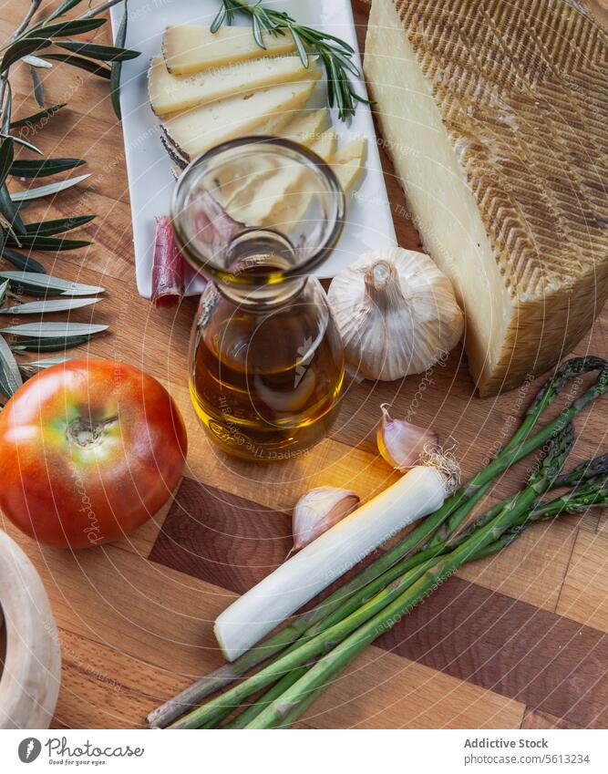 Handwerklich hergestellter Käse und frische Zutaten auf einem Holzbrett Kunstgewerbler Olivenöl Tomate Spargel Knoblauch Zwiebel Schneidebrett hölzern