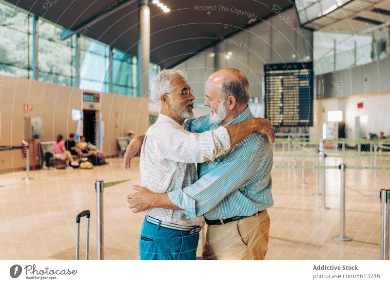 Ältere Reisende umarmen sich auf einem modernen Flughafen Freunde Umarmen Glück Gepäck Seitenansicht Reisender Umarmung Verabschiedung Flugplatz Zusammensein