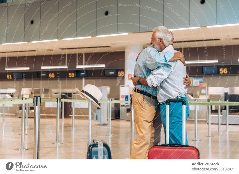 Ältere Reisende umarmen sich auf einem modernen Flughafen Freunde Umarmen Glück Gepäck Seitenansicht Reisender Umarmung Verabschiedung Flugplatz Zusammensein
