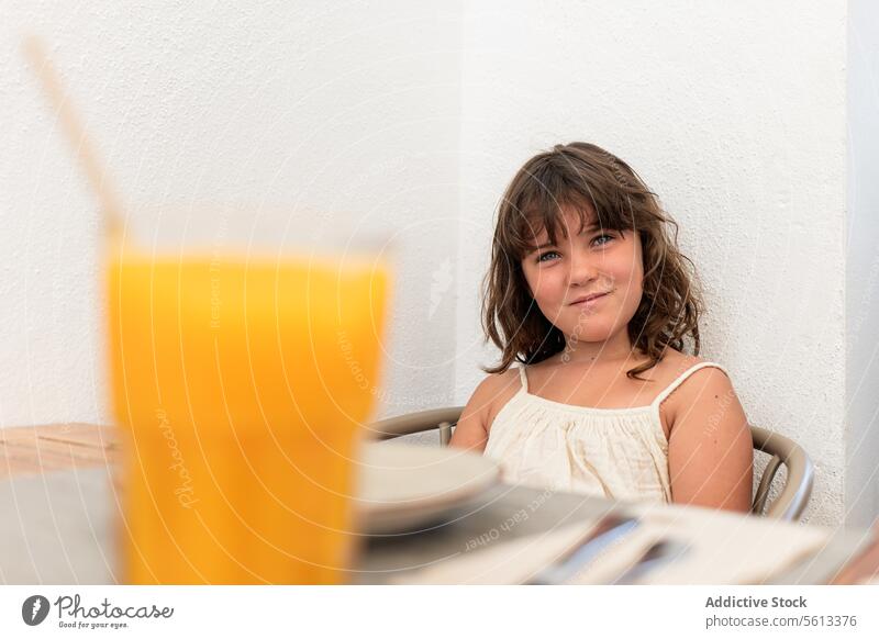 Ruhiges Mädchen mit Getränk sitzt auf einem Stuhl in einem Cafe Porträt Lächeln niedlich Sitzen Wand Café Freizeitkleidung Lifestyle weiß in die Kamera schauen