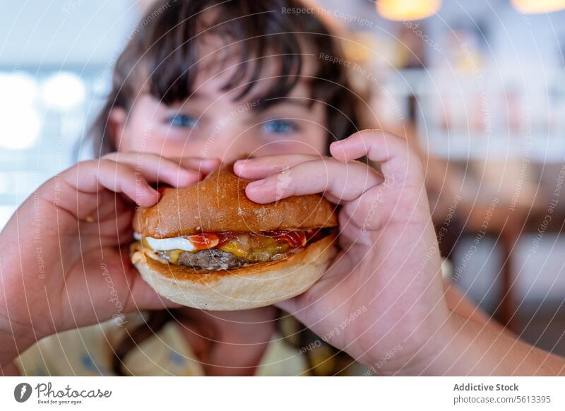 Closeup Hände eines hungrigen anonymen Mädchens, das einen leckeren Hamburger hält und isst und in die Kamera schaut, während es seine Freizeit in einem Café verbringt