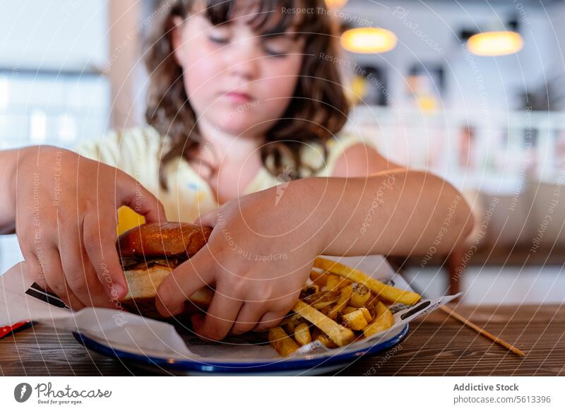 Weibliches Kind isst Burger im Restaurant Mädchen hungrig Hamburger geschmackvoll unschuldig Tisch appetitlich hölzern Mahlzeit Person Lifestyle Kindheit wenig