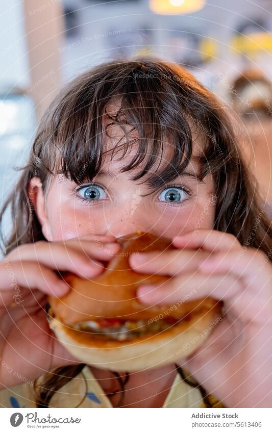Closeup Hände eines hungrigen anonymen Mädchens, das einen leckeren Hamburger hält und isst und in die Kamera schaut, während es seine Freizeit in einem Café verbringt