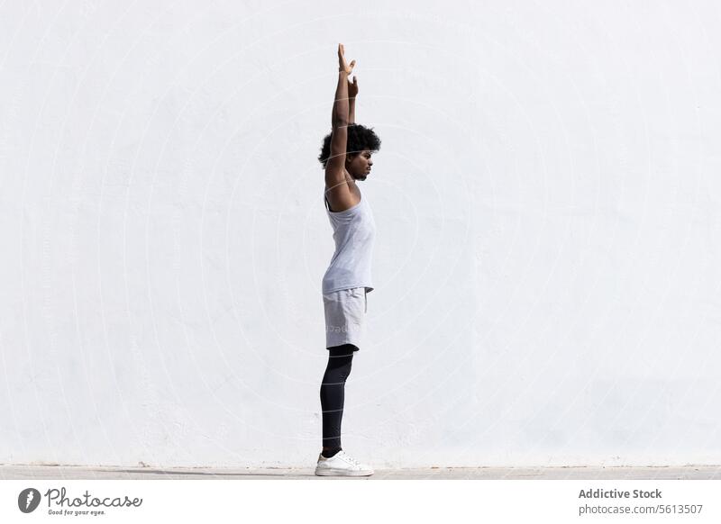 Ganzkörper-Seitenansicht eines selbstbewussten afroamerikanischen männlichen Sportlers in Sportkleidung, der konzentriert die Arme ausstreckt, während er vor einem weißen Hintergrund steht und wegschaut