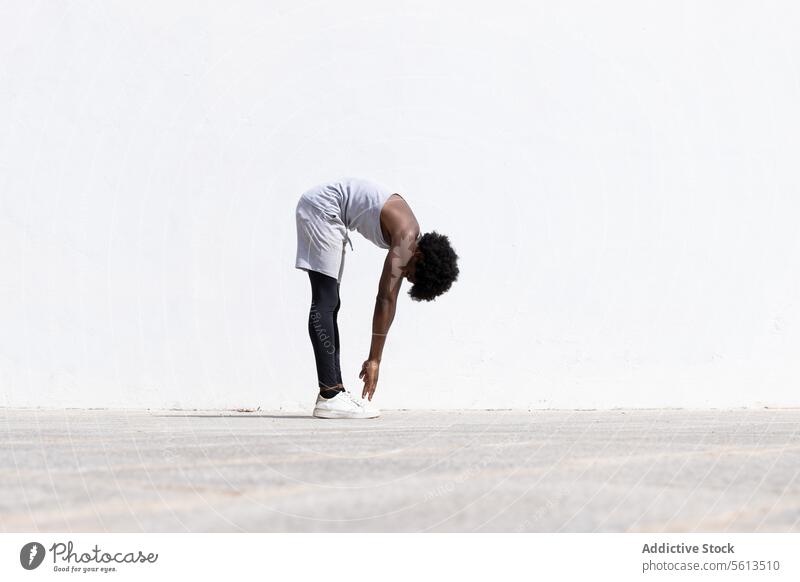 Schwarzer Sportler streckt seinen Körper auf der Straße Athlet Mann Übung Afrohaar Wegbiegung Bestimmen Sie Sportbekleidung Dehnung Arme weiß Wand Seitenansicht