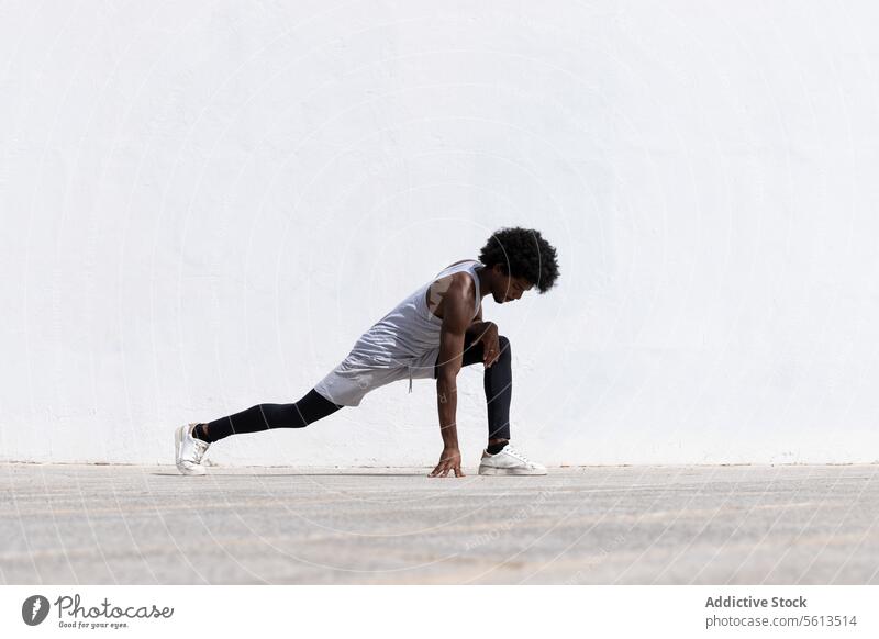 Seitenansicht eines konzentrierten schwarzen männlichen Sportlers in Sportkleidung und Turnschuhen, der seinen Körper streckt, während er sich auf der Straße beim Fitnesstraining in der Stadt bückt