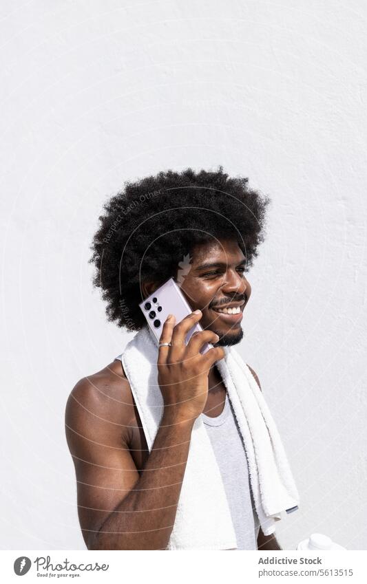 Männlicher Sportler beim Telefonieren auf weißem Hintergrund Athlet Mann Übung Afrohaar Lächeln Anruf Mobile reden Handtuch Wegsehen Mitteilung aktiv Wand Glück