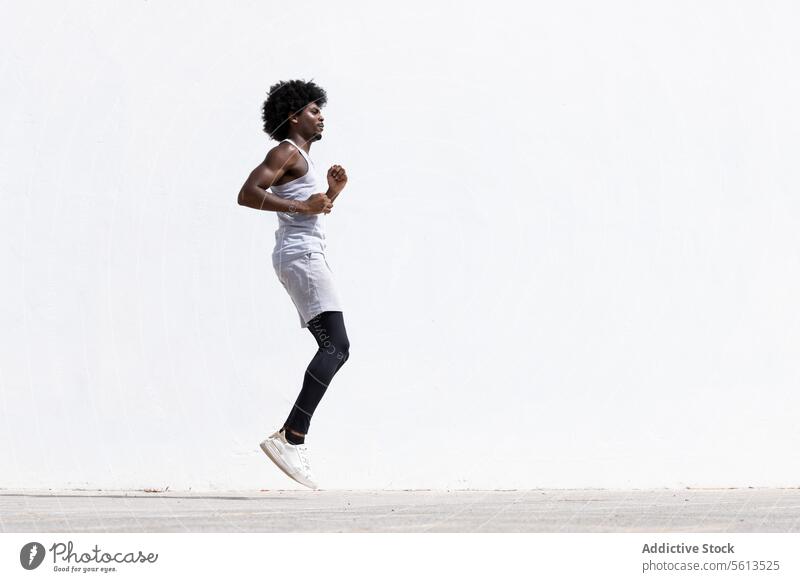 Seitenansicht eines entschlossenen jungen aktiven afroamerikanischen männlichen Sportlers in Sportkleidung, der während eines Fitnesstrainings auf der Straße gegen eine weiße Wand springt