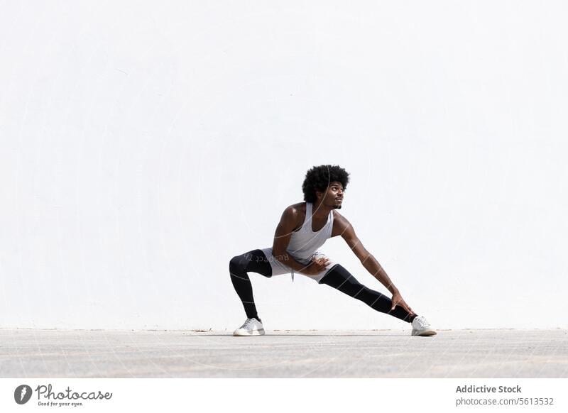 Konzentrierter schwarzer männlicher Sportler in Sportkleidung und Turnschuhen, der seinen Körper auf der Straße beim Fitnesstraining in der Stadt dehnt Athlet