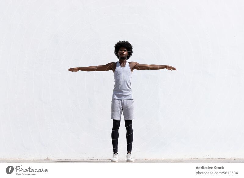 Ganzkörperdarstellung eines selbstbewussten afroamerikanischen männlichen Sportlers in Sportkleidung, der konzentriert die Arme ausstreckt, während er vor einem weißen Hintergrund steht und wegschaut