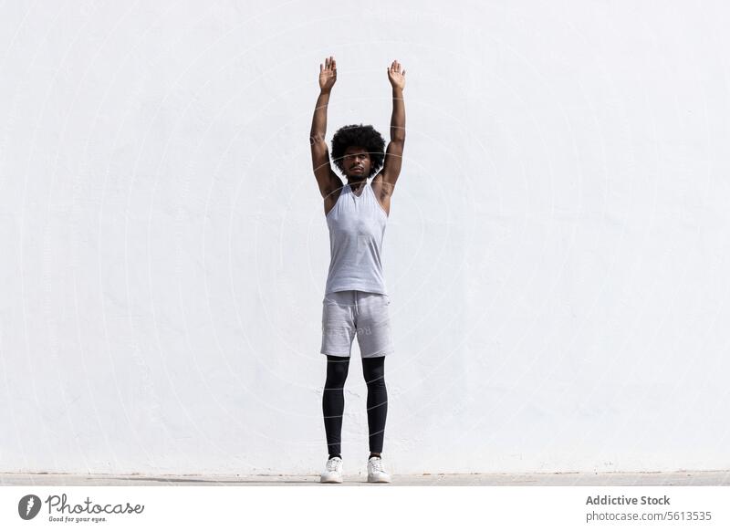 Ganzkörperdarstellung eines selbstbewussten afroamerikanischen männlichen Sportlers in Sportkleidung, der konzentriert die Arme ausstreckt, während er vor einem weißen Hintergrund steht und wegschaut