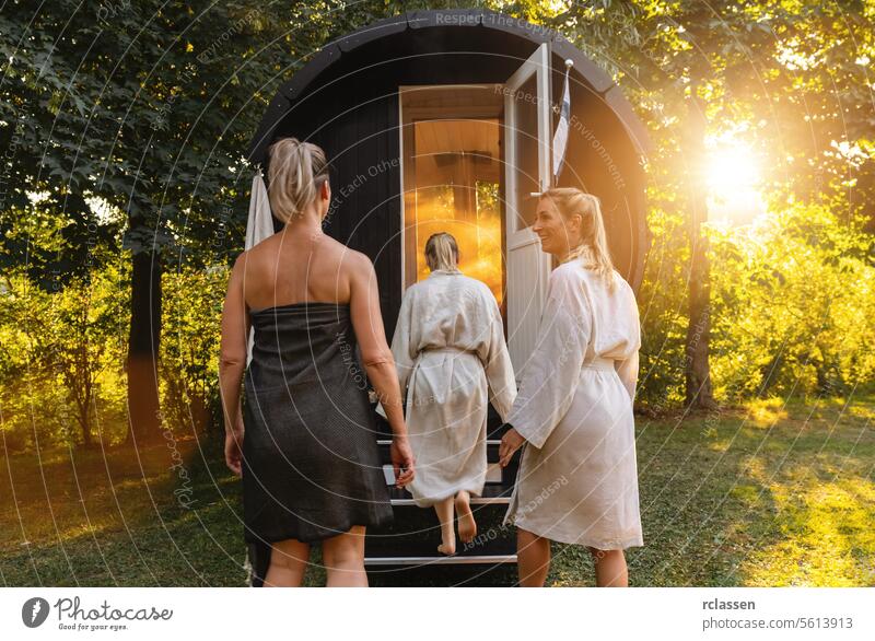 Drei Menschen in Gewändern gehen in ein finnisches Saunafass in einem sonnenbeschienenen Wald bei Sonnenuntergang Frau glückliche Menschen Holzfass Mobile